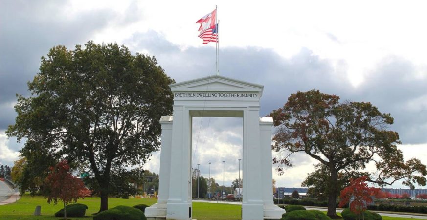 Peace Arch monument with Canadian and U.S. flags above, framed by trees at Peace Arch Park on the Canada–U.S. border.